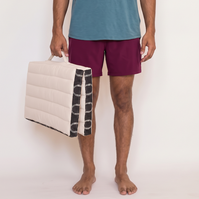 Man carrying a folded ivory and black Kosha meditation cushion by its handle