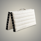 Folded ivory and black meditation cushion standing on its edge with its fabric carry handle on top
