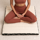 Woman sitting cross-legged on an open ivory and black meditation cushion, knees and ankles supported