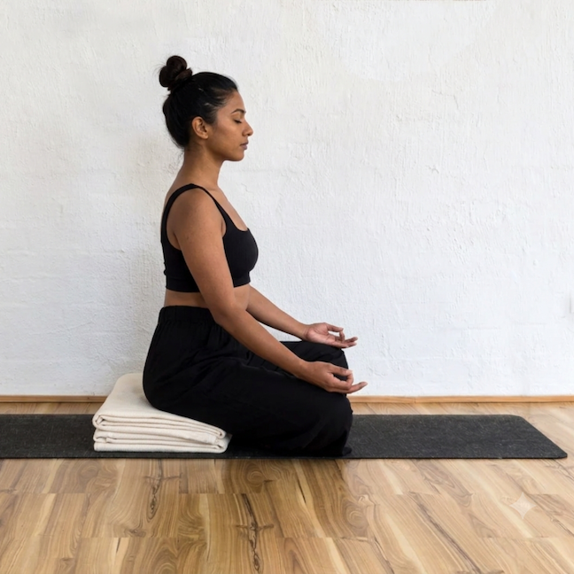 Woman meditating cross-legged on a folded natural cotton yoga blanket used as a meditation seat