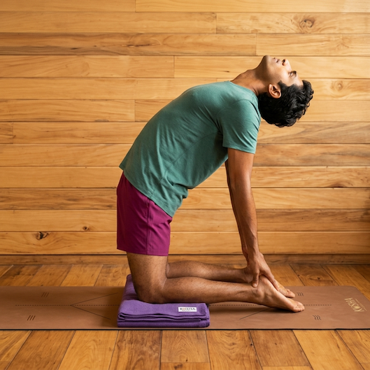 Man in camel pose kneeling on a folded purple Kosha yoga blanket to cushion his knees